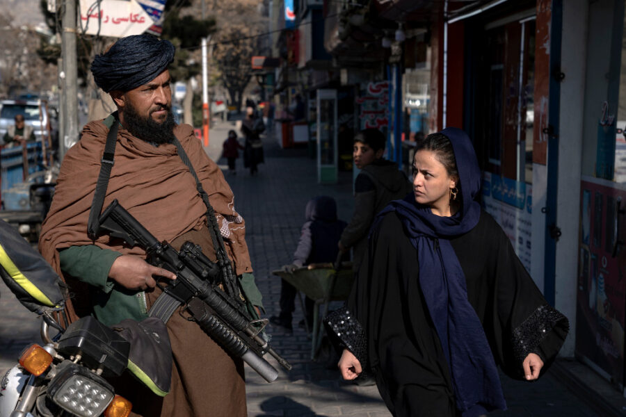 En talibansk stridande står vakt medan en kvinna passerar i Kabul, Afghanistan i december 2022.