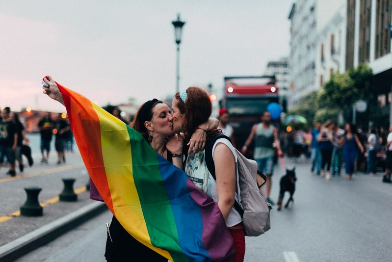 Två unga kvinnor kramar varandra och en av dem håller i en regnbågsfärgad flagga.