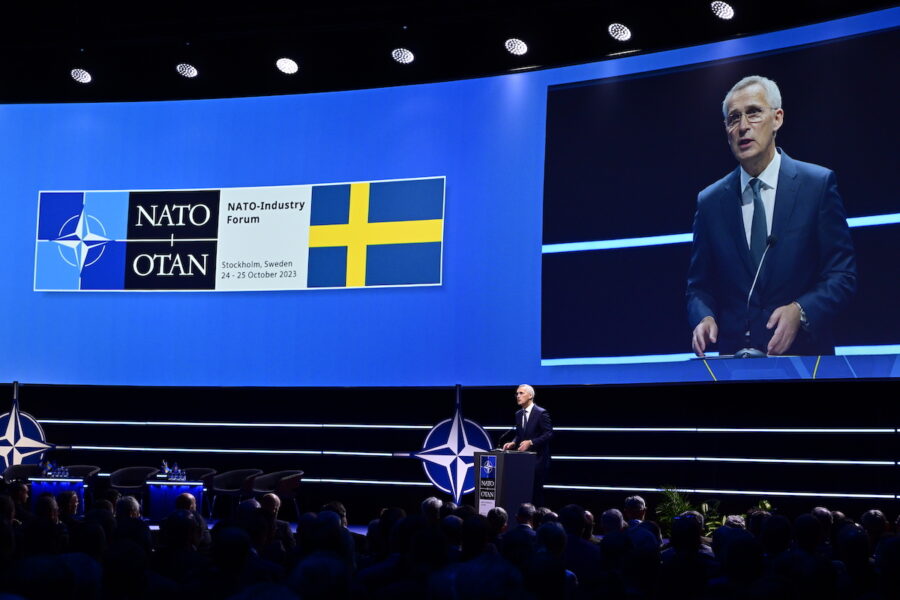 Jens Stoltenberg talar inför publik. Sveriges flagga och Natos emblem visas på en skärm.