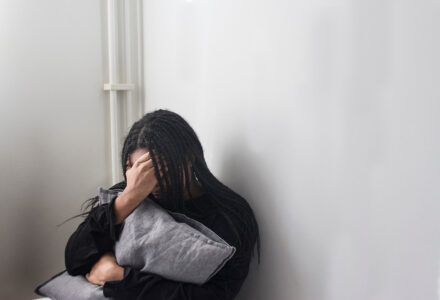 Ung kvinna kramar en kudde, håller handen för ansiktet.