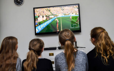 Fyra flickor sitter med ryggen åt kameran och tittar på en tv-skärm.