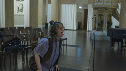 Sara Parkman står framåtlutad med hörlurar och tungan ute