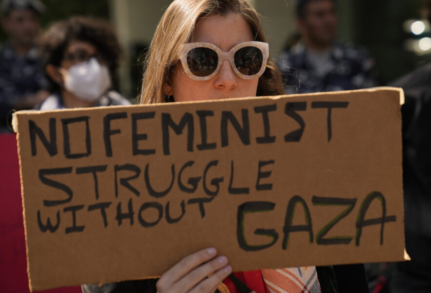 Kvinna med solglasögon håller en kartongbit där det står: No feminist struggle without Gaza