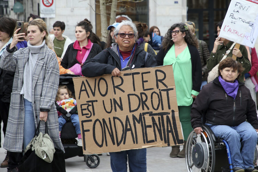 Kvinna håller en skylt för aborträtt i Frankrike. Flera andra kvinnor runtomkring.