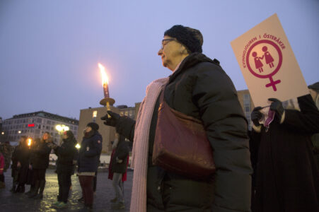 Kvinna i kappa och hatt håller ett ljus i handen