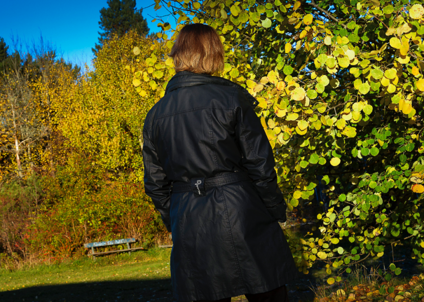 Kvinna vänd mot gulnande lövträd med ryggen mot kameran.