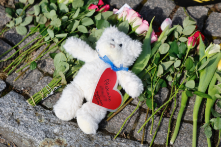 Liten vit nalle ligger på en bädd av rosor på marken.