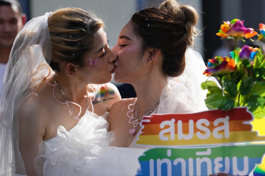 två kvinnor kysser varandra med ett regnbågsplakat i förgrunden.