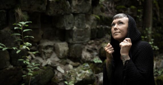 Emma Kronborg i svarta kläder med skog i bakgrunden