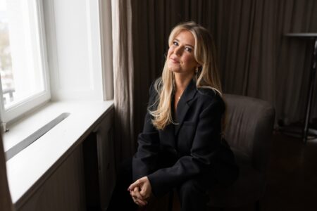 Kvinna i svart kostym sitter vid ett fönster.