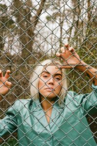 Maxida Märak i grön skjorta bakom ett stängsel