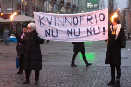 Kvinnor håller i en rosa banderoll och i varsin fackla med budskap om kvinnofrid.