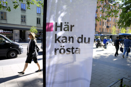 Informationsskylt Här kan du rösta och människor som går på gatan bakom