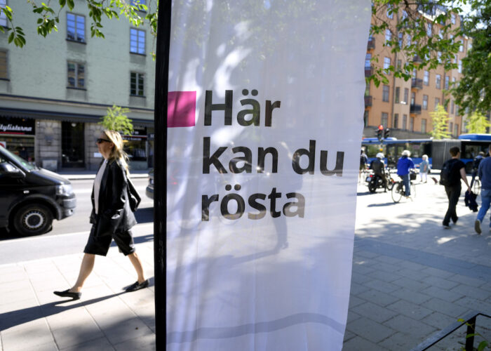 Informationsskylt Här kan du rösta och människor som går på gatan bakom