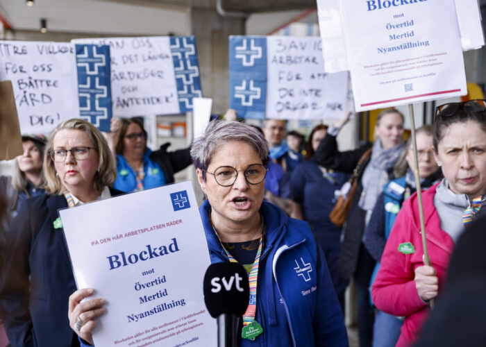 Demonstranter varav en kvinna i mitten håller i en skylt med Vårdförbundets logga där det står på den här arbetsplatsen råder blockad