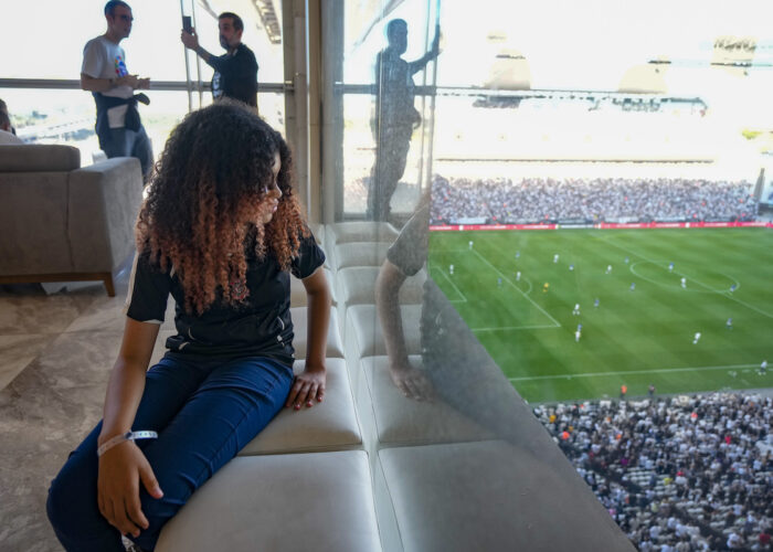 flicka sitter i ett rum med fönster och tittar på en fotbollsmatch nedanför
