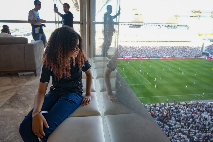 flicka sitter i ett rum med fönster och tittar på en fotbollsmatch nedanför