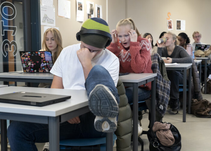 Trötta elever i ett klassrum. En har handen för ansiktet och benet på bänken. En elev dricker ur en pappersmugg en annan håller händerna vid huvudet