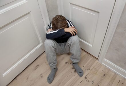 pojke sitter i ett hörn med huvudet ner och armarna över ansiktet