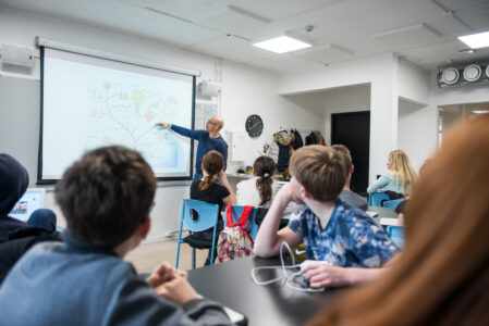 elever sitter och tittar på tavlan där en man står och förklarar något