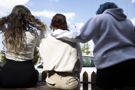 tre unga tjejer sitter på en bänk ute med ryggen mot kameran