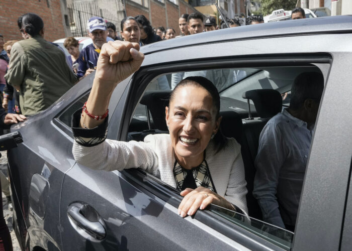 Claudia Sheinbaum lutar sig ut från fönstret i bilen med höjd högerhand och knuten näve