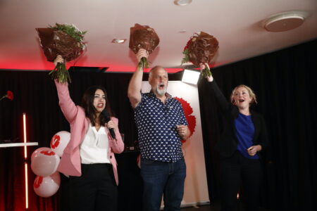Tre personer på en scen har höjt armen med en blombukett i handen och ser glada ut