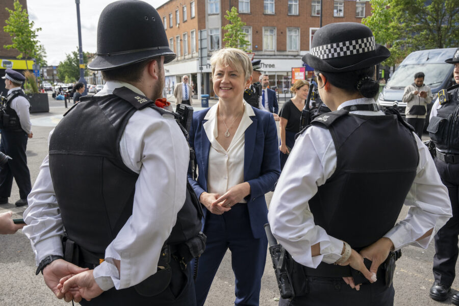 Blond korthårig kvinna och ryggen på två poliser i brittisk polisuniform