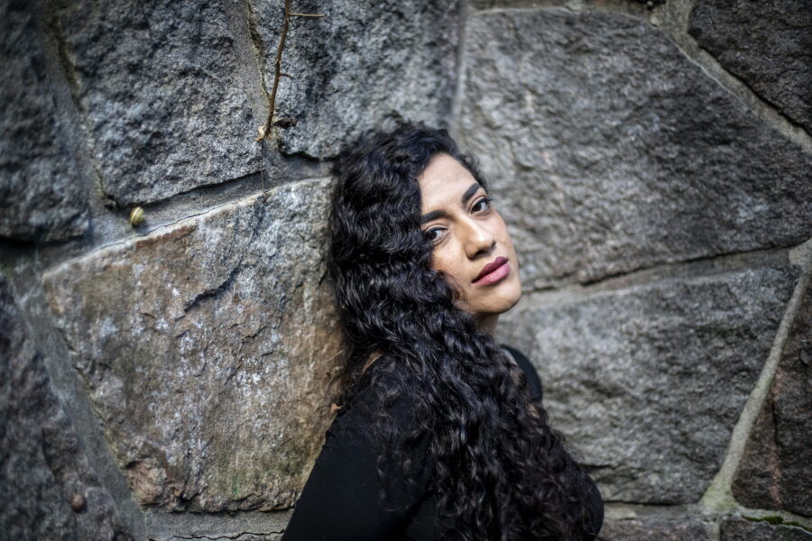 Porträtt av Athena Farrokhzad i svart tröja och utsläppts långt hår mot en stenmur