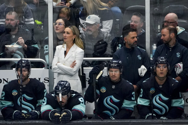 Kvinna klädd i vitt i ett hockyebås fullt med hockeyspelare