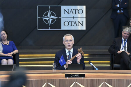 Jens Stoltenberg sitter ner, bakom syns Natoflaggan