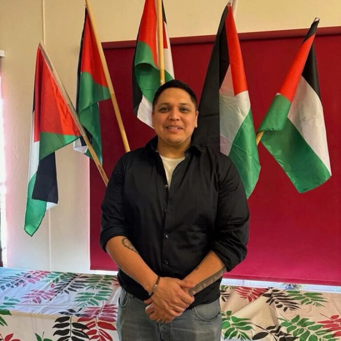 Man i svart skjorta framför flera Palestinaflaggor.