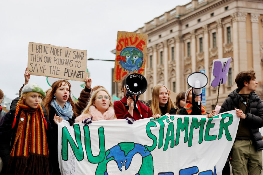 Unga i demonstrationståg med banderoll och plakat.