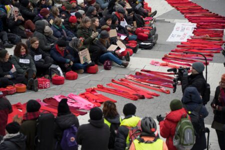 Kvinnor sitter på marken med röda stickade halsdukar framför sig.