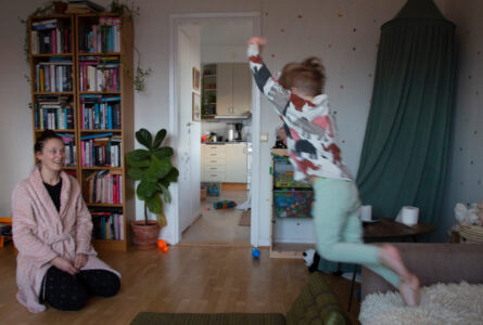 En kvinna sitter på golvet och tittar på ett barn som hoppar från en soffa.