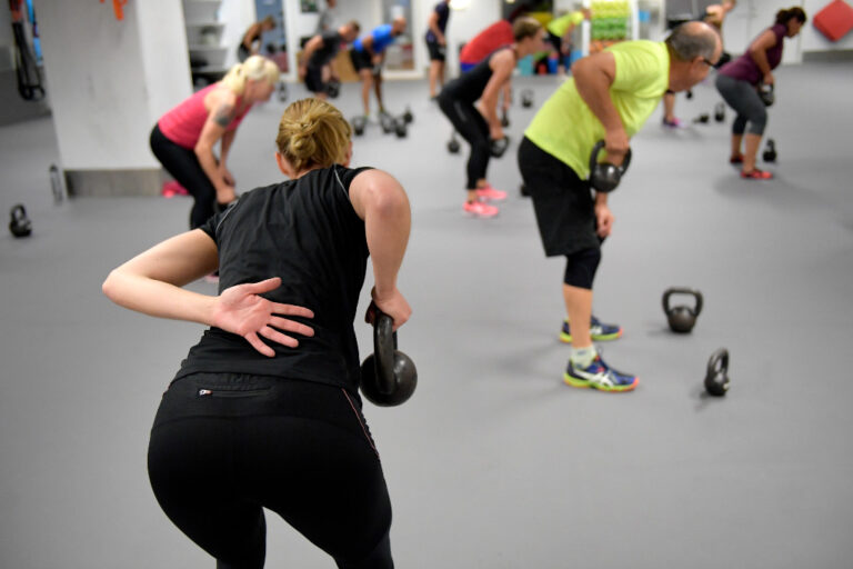 Ryggtavla på kvinna i svart som tränar med kettlebell.