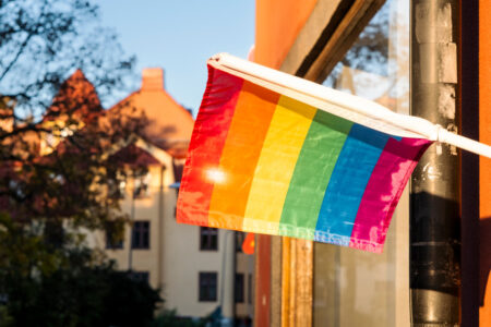 Prideflagga hänger på husfasad i solljus.