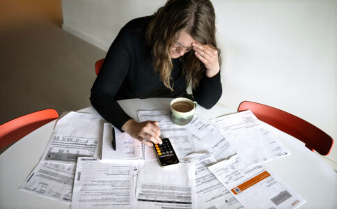 Kvinna med miniräknare och räkningar utspridda på bord.