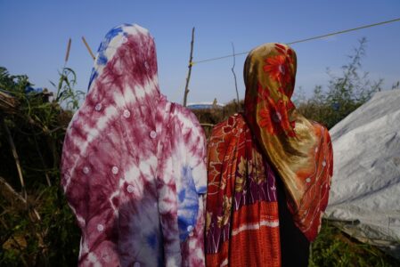 Två kvinnor i färgglada sjalar står med ryggen åt kameran.