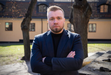 Peter Sidlund Ponkala med armarna i kors framför två träd och en gul byggnad i bakgrunden.