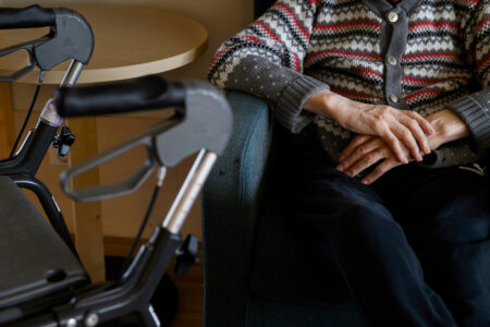 Äldre person sitter med rullator bredvid sig.