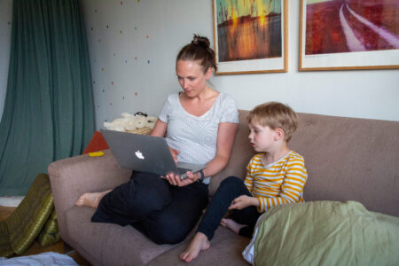 Mamma och barn tittar på dator i en soffa.