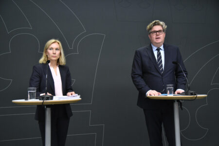 Viveca Lång och Gunnar Strömmer står vid varsitt bord med mörk bakgrund.