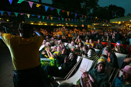 Fotbollssupportrar sitter i solstolar och tittar på EM utomhus.