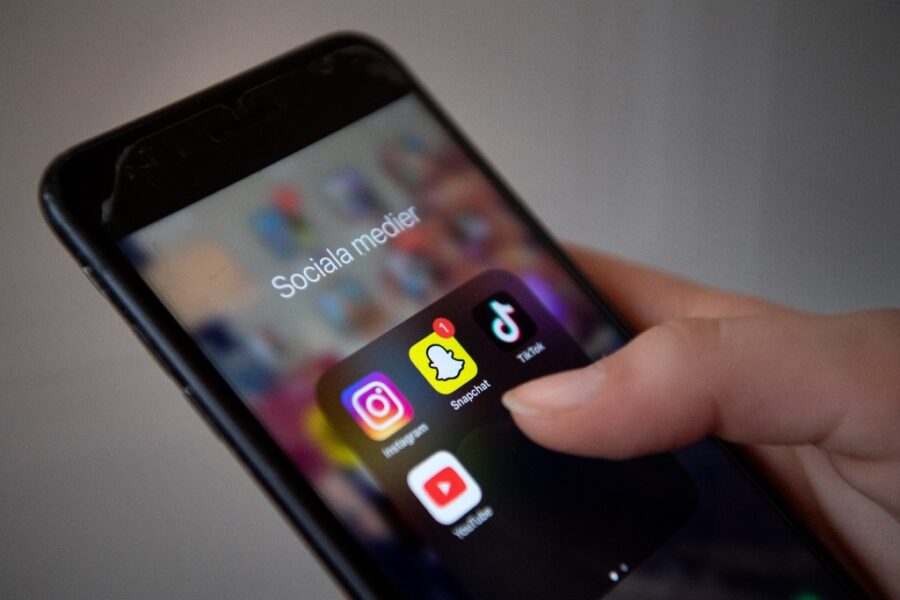 Hand håller i mobil där apparna Instagram, Snapchat, Tiktok och Youtube syns.