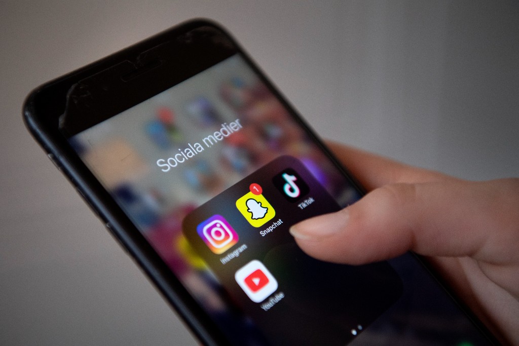 Hand håller i mobil där apparna Instagram, Snapchat, Tiktok och Youtube syns.