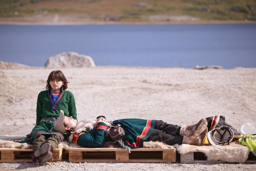 Två personer i samisk klädsel sitter och ligger ner.