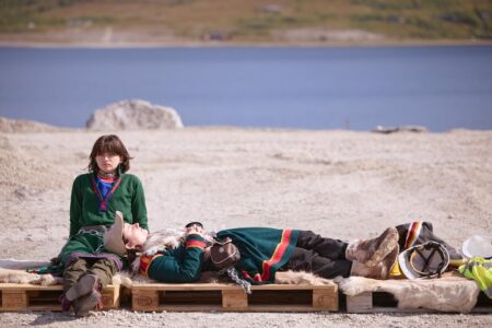 Två personer i samisk klädsel sitter och ligger ner.