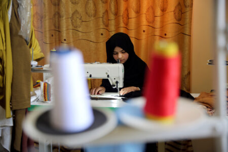 Ung afghansk kvinna i svart sitter vid symaskin.