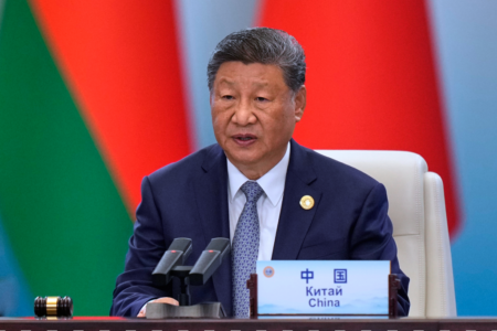 Xi Jinping sitter vid ett konferensbord med mikrofon och skylt.